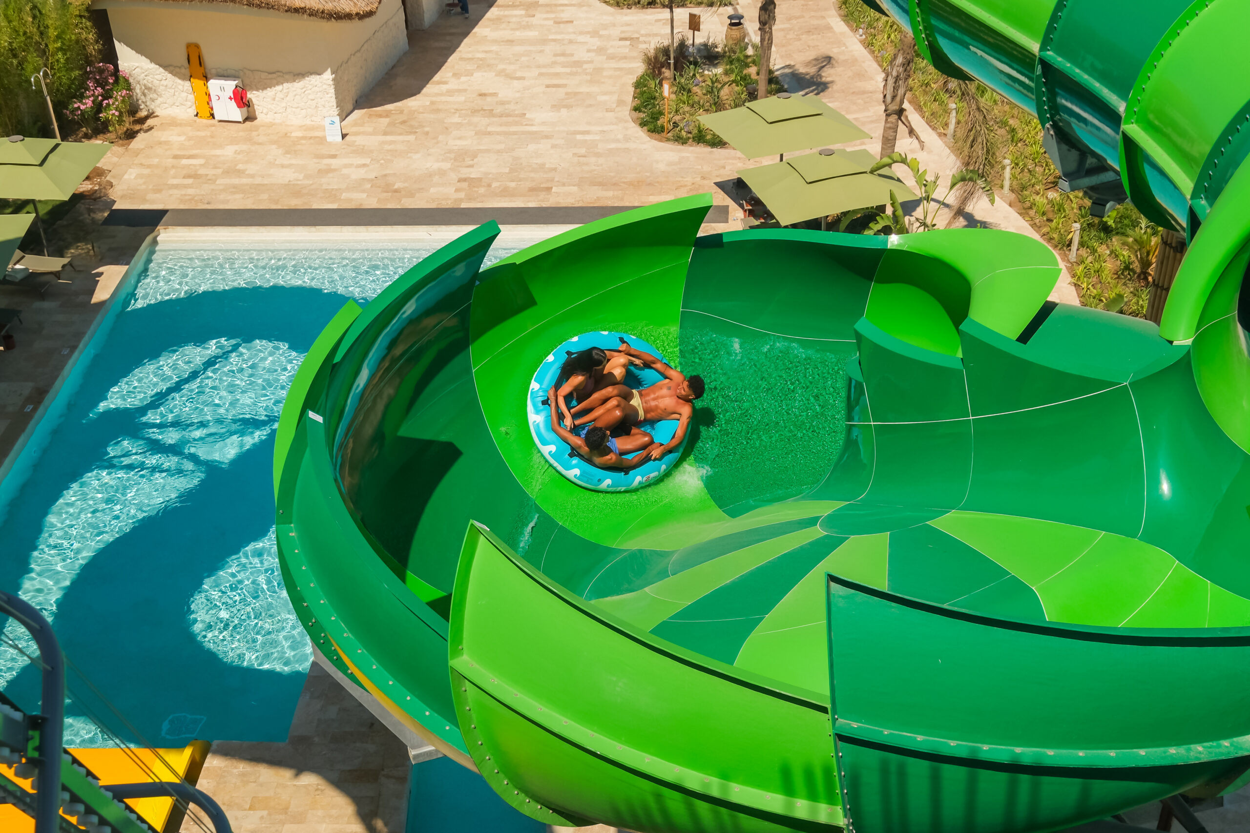 Three people in a raft in a green, bowl-like water slide