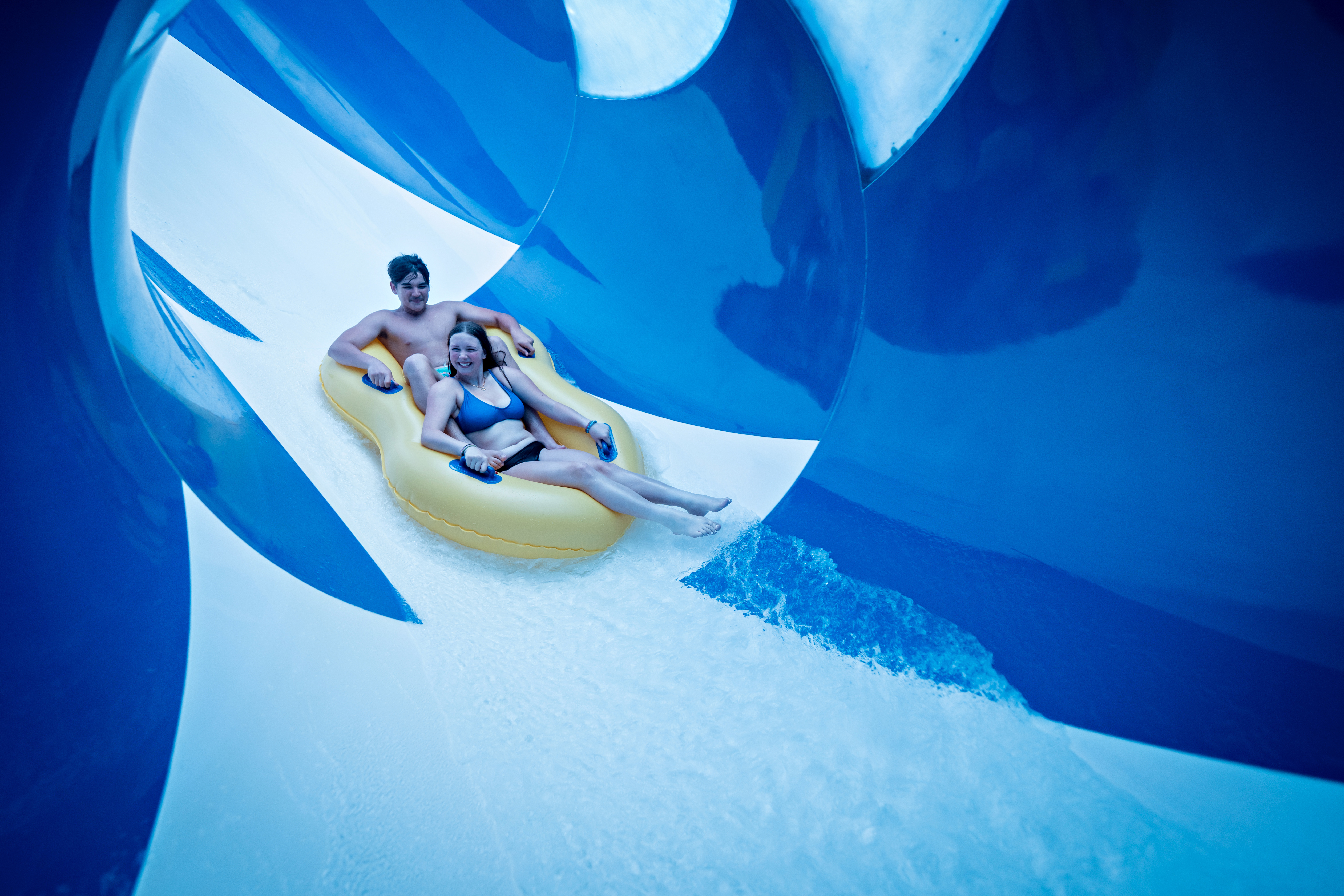 Two riders on an inner tube inside a water slide flume