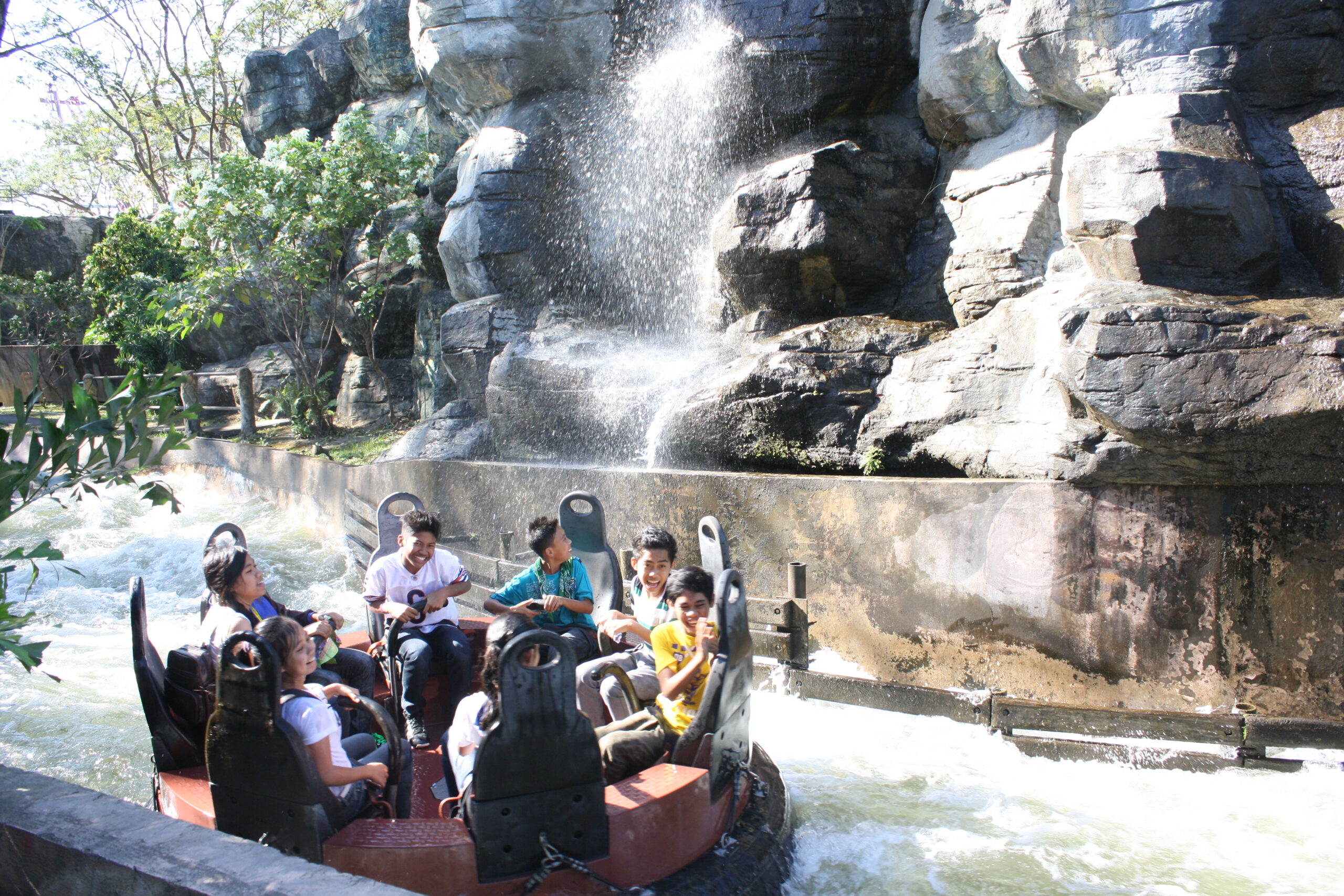 A river raft ride boat with riders, against an artificial waterfall