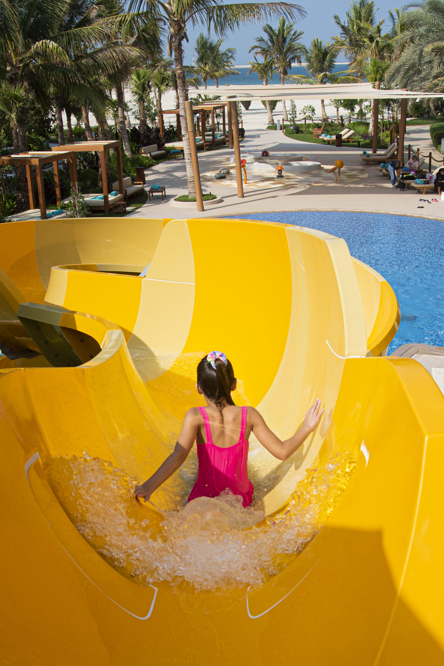 The back of a little girl going down a yellow water slide
