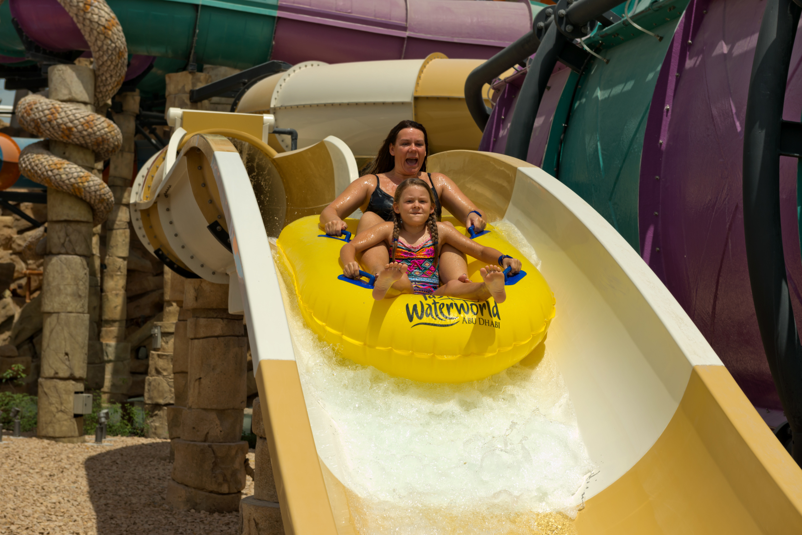 woman and girl on inner tube going down yellow water slide