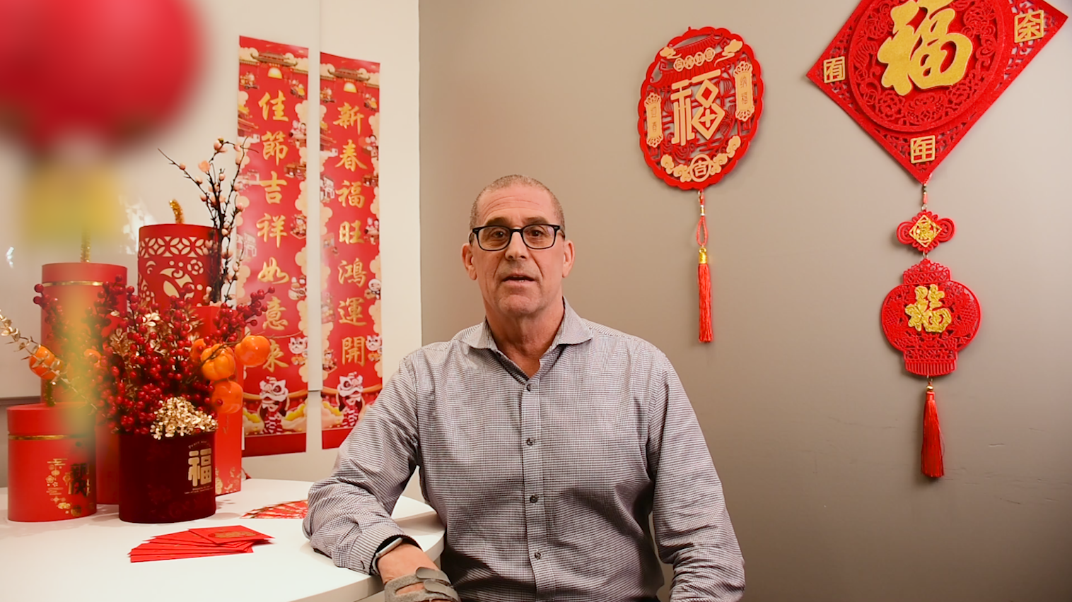 Man speaking with red Chinese New Year decorated backdrop