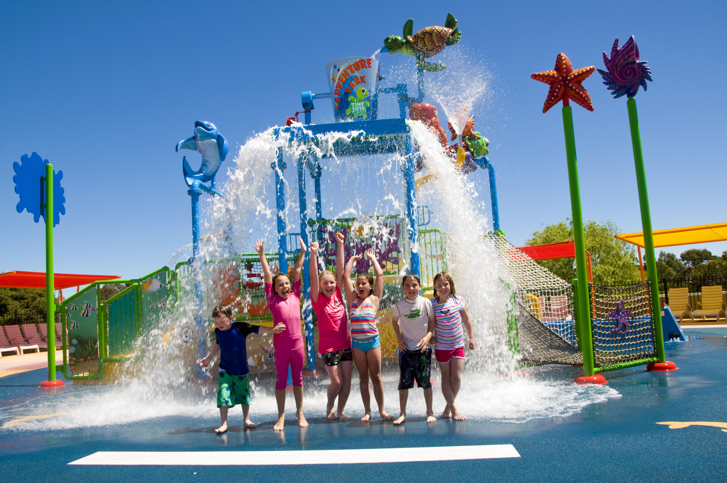 Children jumping under a bucket tipping water from an aquatic play structure