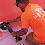 A man in an orange shirt holding a buffer buffing a water slide