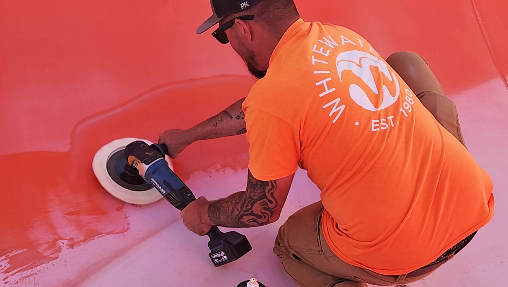A man in an orange shirt holding a buffer buffing a water slide