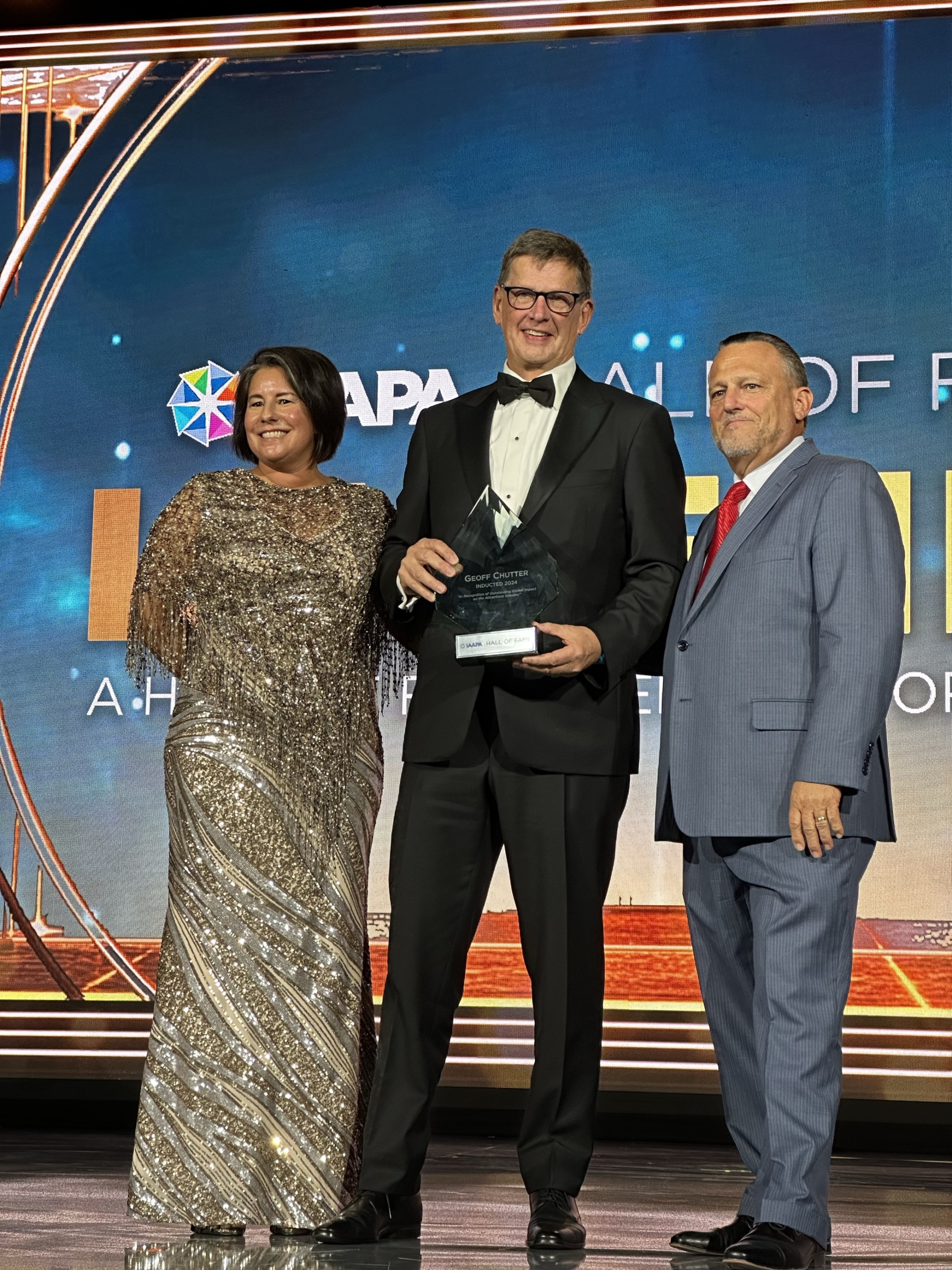 Three people on stage with the man in the middle receiving an award