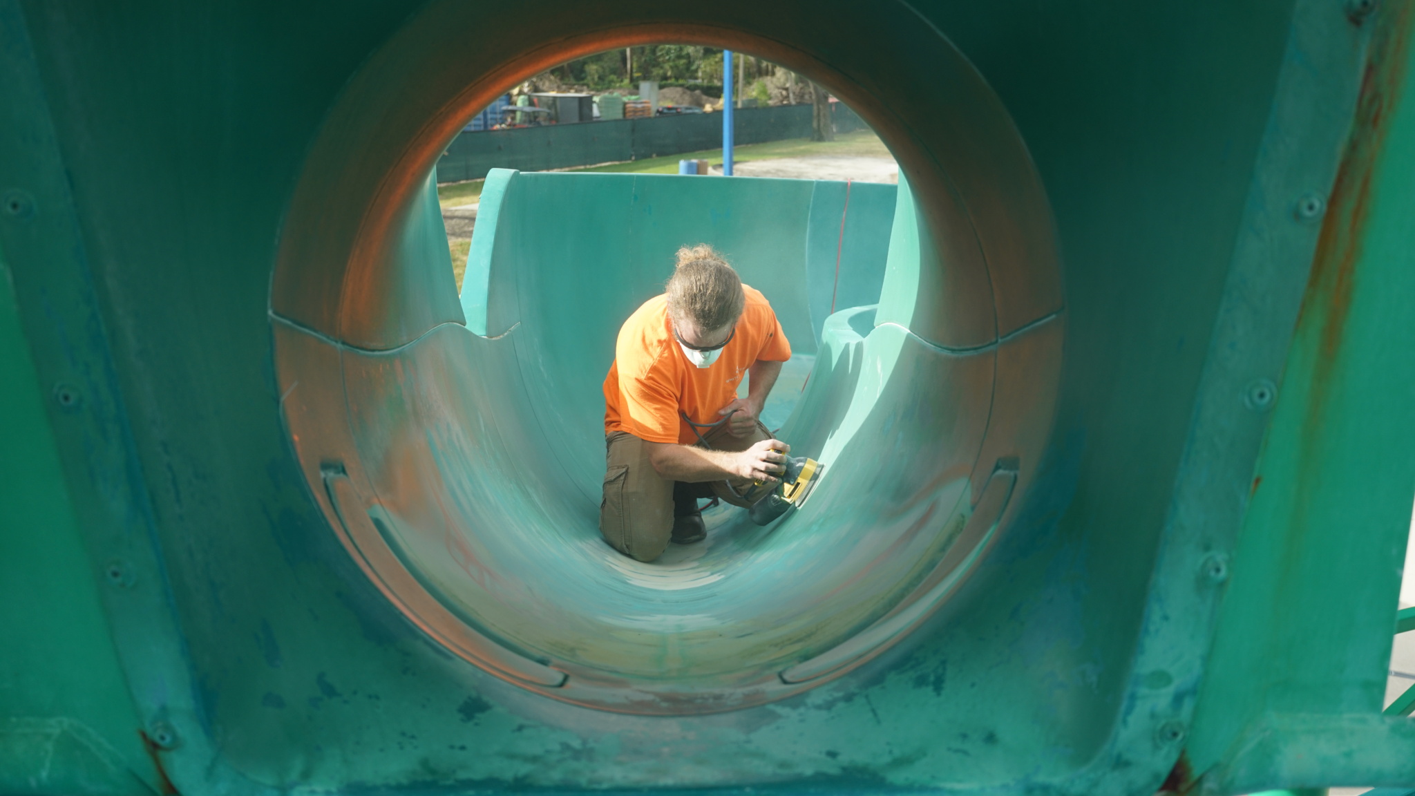 Man refinishing the inside of a green enclosed water slide