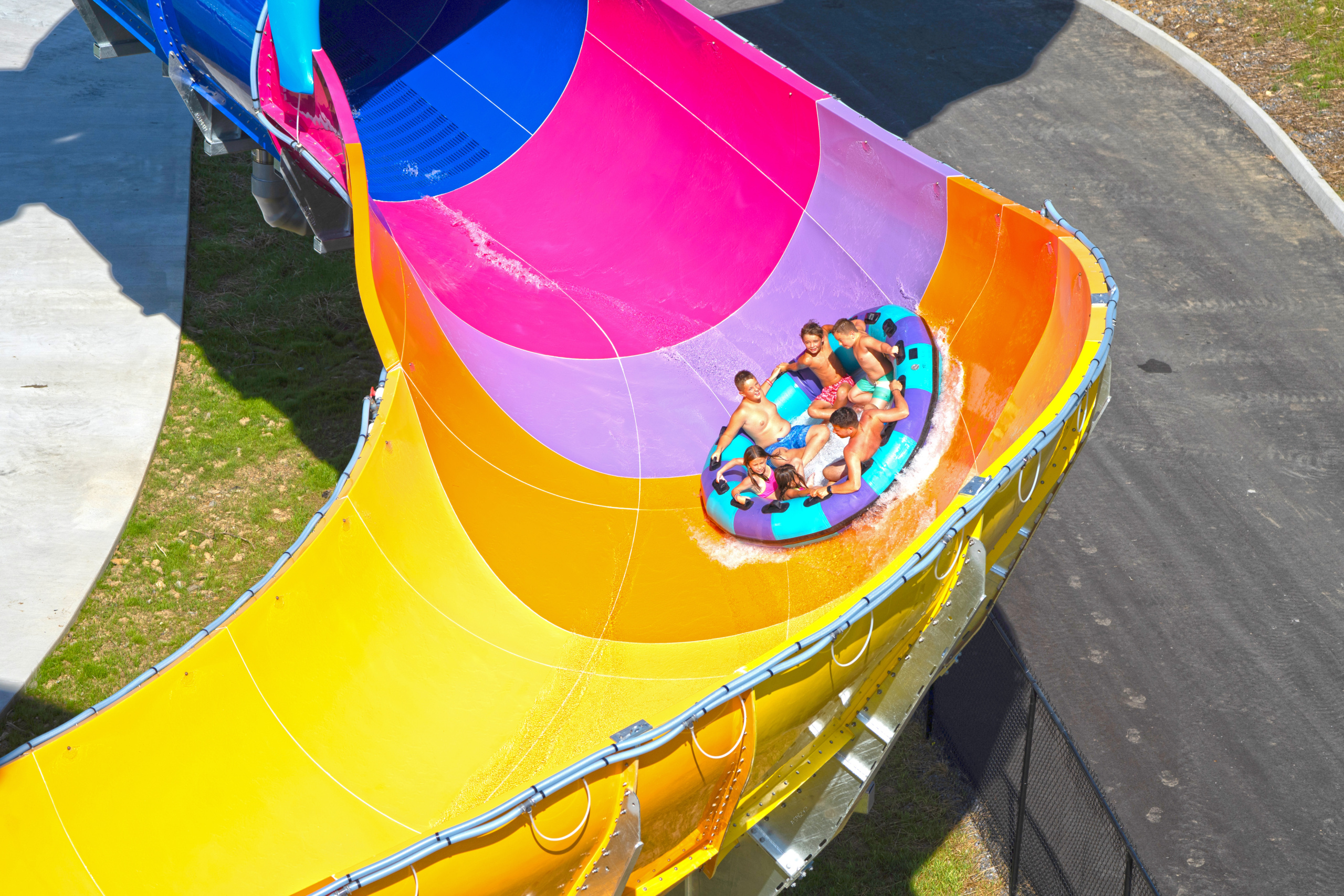 Drone shot of a family raft of 6 people racing high up on the blue, pink, purple, orange, and yellow Wall Runner wall.