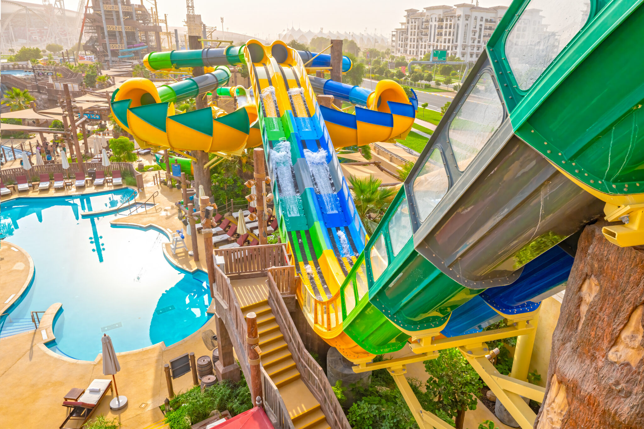 A view from the deck, down the side of a green, blue, and yellow Blaster Battle water slide at Yas Waterworld.