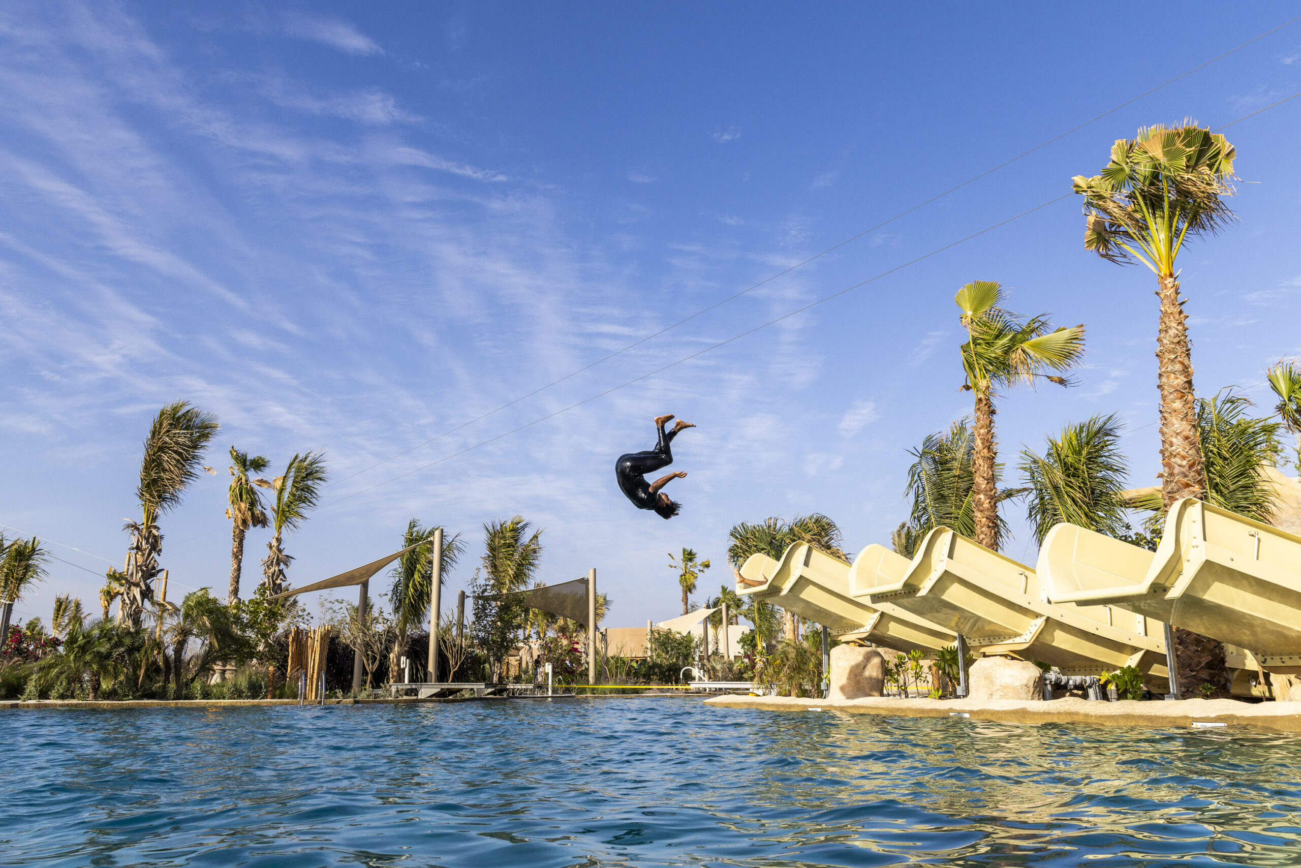 Person doing back flip in the air flying off one of three beige water slides