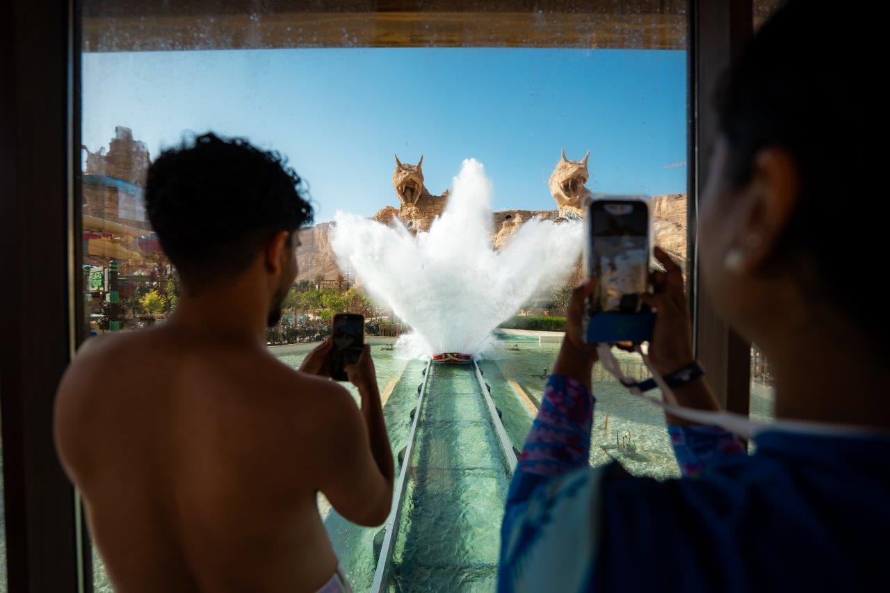 Two people taking picture of a huge splash stemming from a Shoot the Chute ride