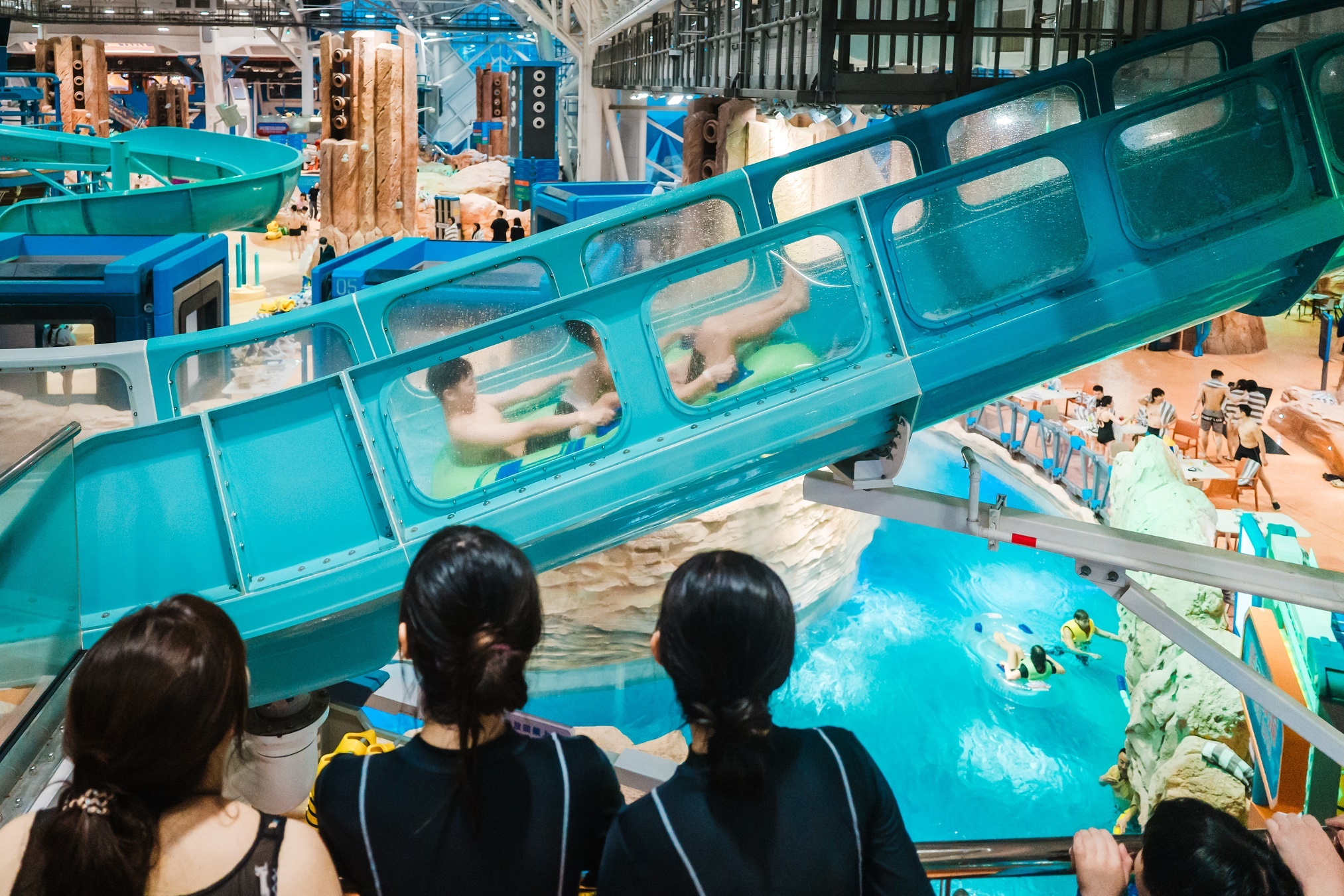 Three women watching riders in an inner tube inside a water coaster
